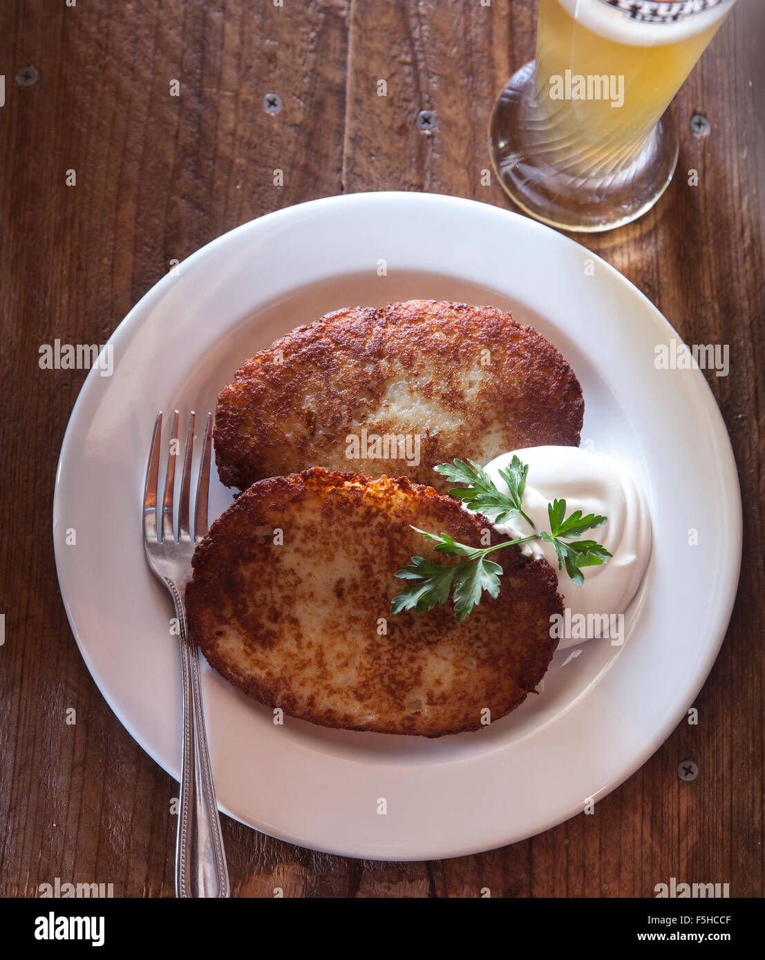 looking down on a plate with two potato latkes and sour cream and beer Stock Photo