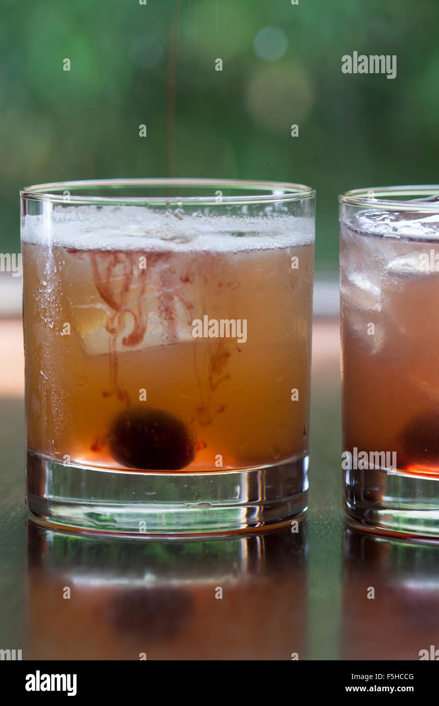 Two iced cocktails with cherries in short glasses with foliage in the background Stock Photo