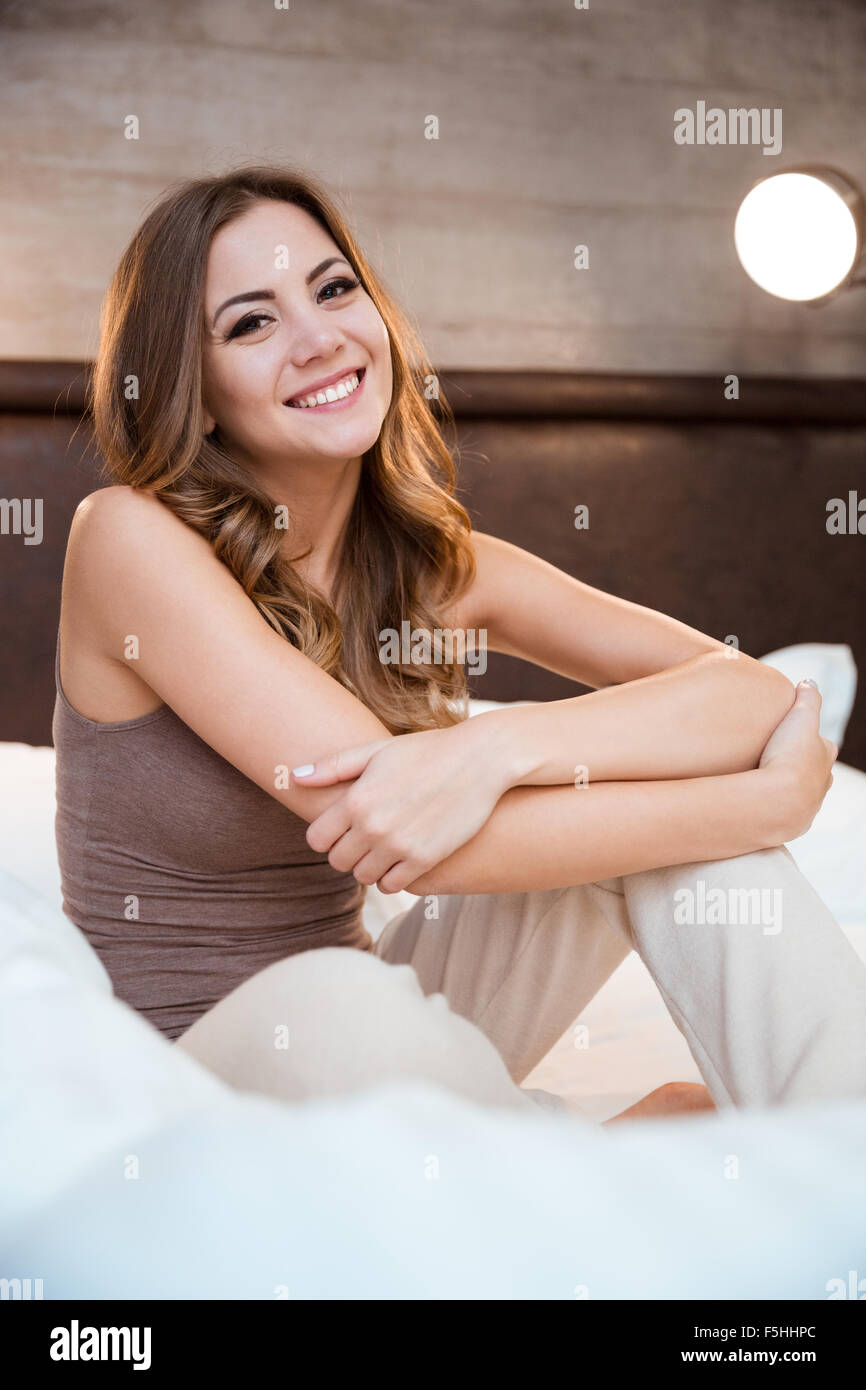 Beautiful young curly smiling woman sitting on a bed in pajamas Stock Photo