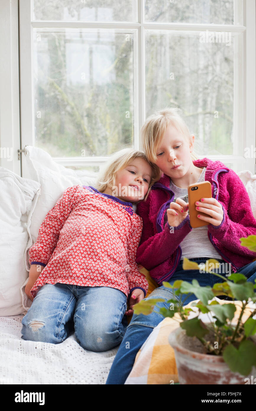 Sweden, Sisters (4-5, 10-11) using smart phone at home Stock Photo