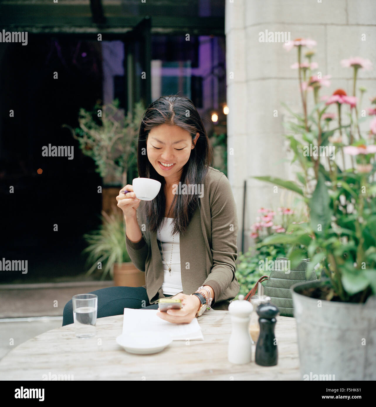 Sweden, Stockholm, Ostermalm, Smiling woman sitting at sidewalk cafe and text messaging Stock Photo