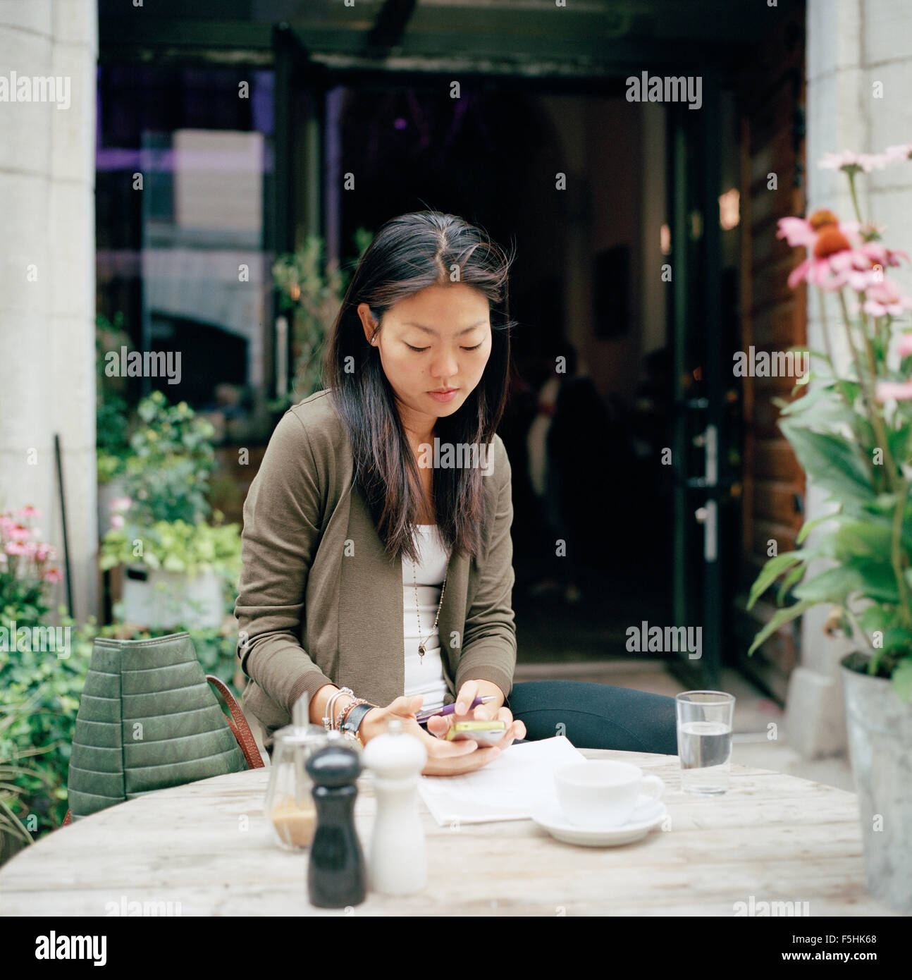 Sweden, Stockholm, Ostermalm, Woman sitting at sidewalk cafe and text messaging Stock Photo