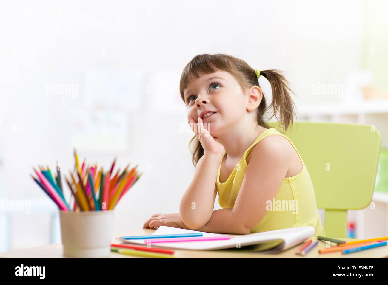 Cute dreamy kid girl drawing with color pencils in nursery Stock Photo