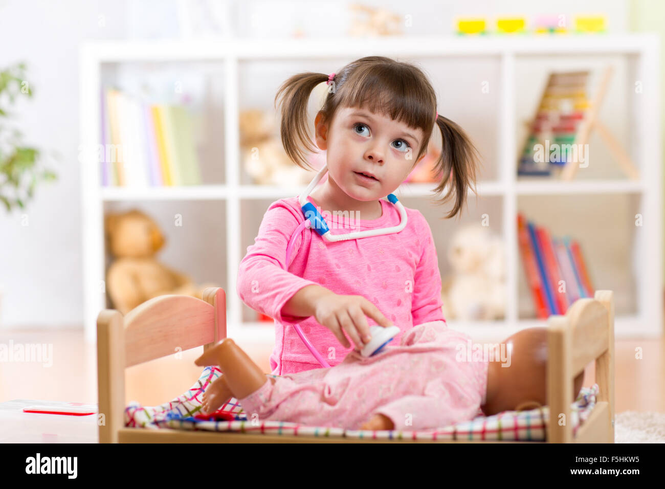 Child girl plays doctor examining baby doll patient with toy stethoscope Stock Photo