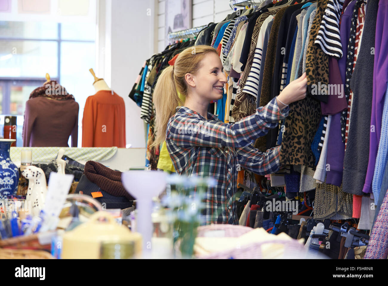 Female Shopper In Thrift Store Looking At Clothes Stock Photo