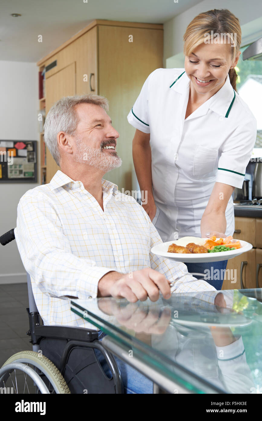 Carer Serving Meal To Man In Wheelchair At Home Stock Photo