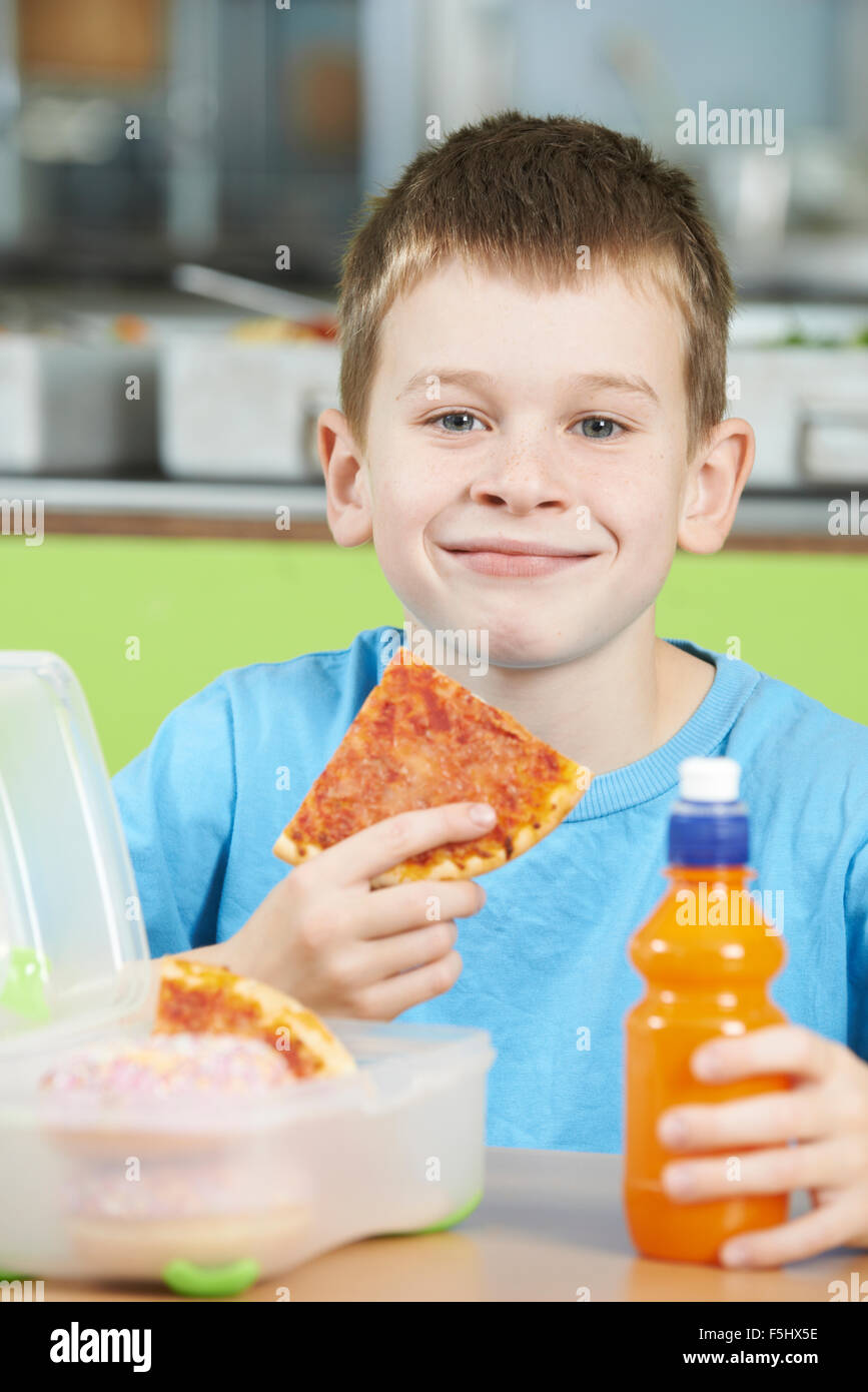 Male Pupil Sitting At Table In School Cafeteria Eating Unhealthy Packed Lunch Stock Photo