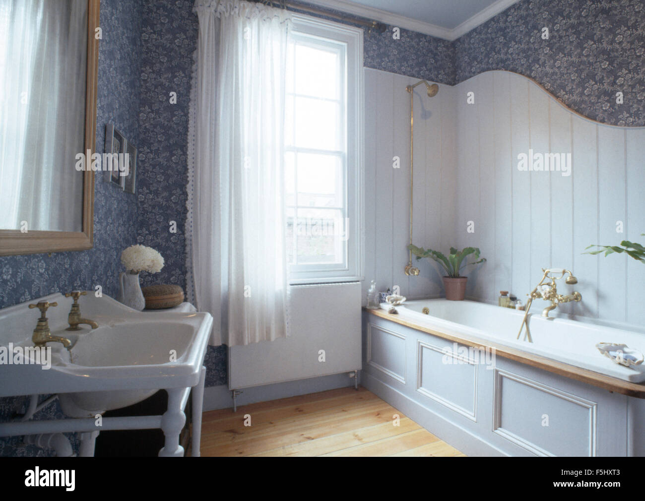 White tongue+groove panelling above bath in seventies bathroom with blue floral wallpaper Stock Photo