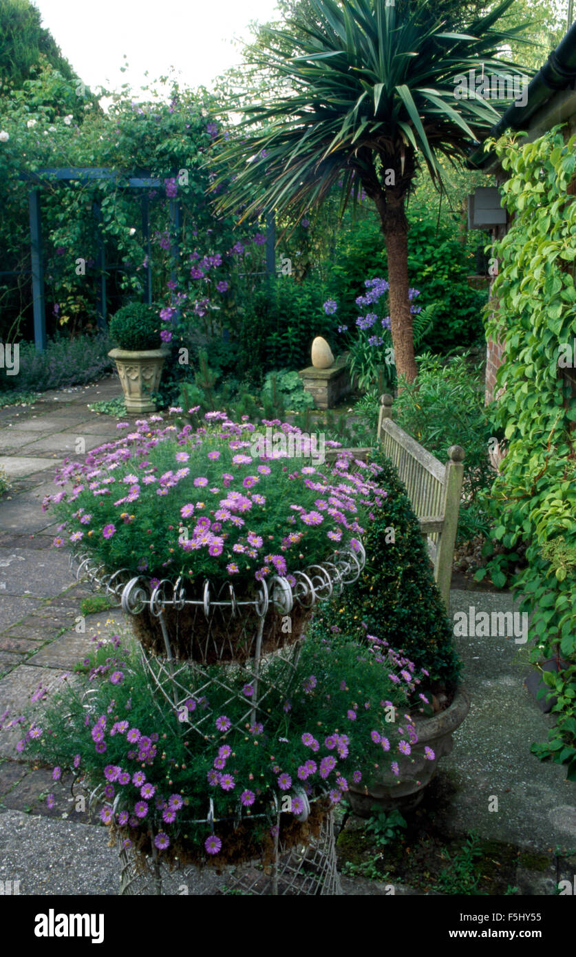 Blue flowered annuals in tiered wirework baskets on terrace in country garden Stock Photo