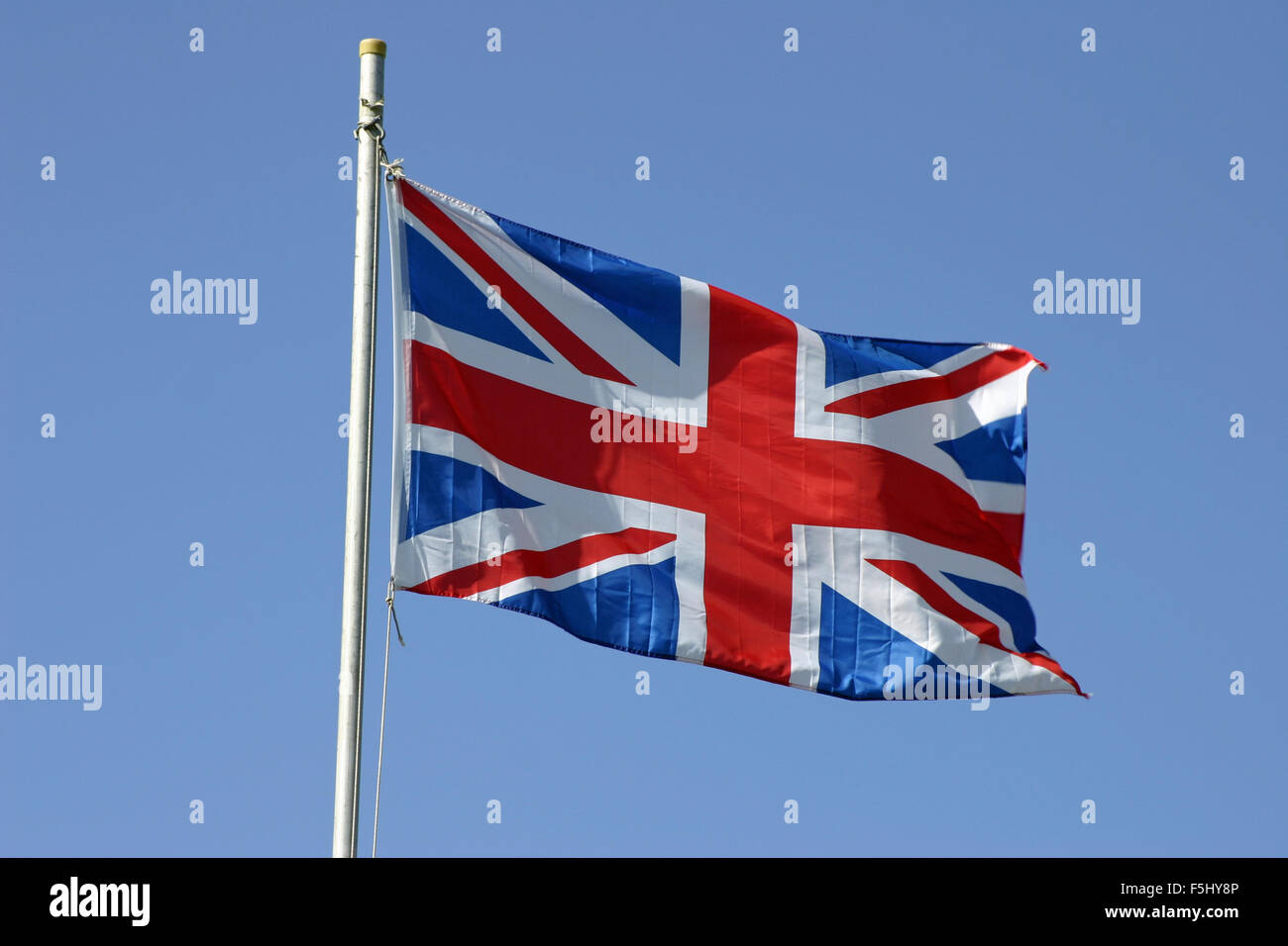 Union Jack flag flying on a flagpole in the wind against a blue sky ...