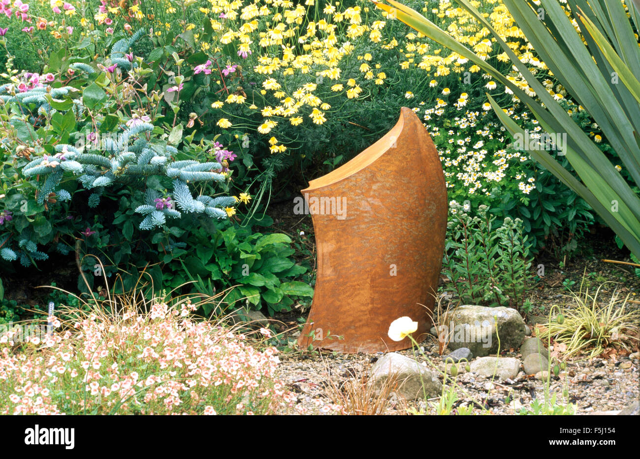 Modern sculpture in front of a summer border with yellow Anthemis and a dwarf blue Spruce Stock Photo