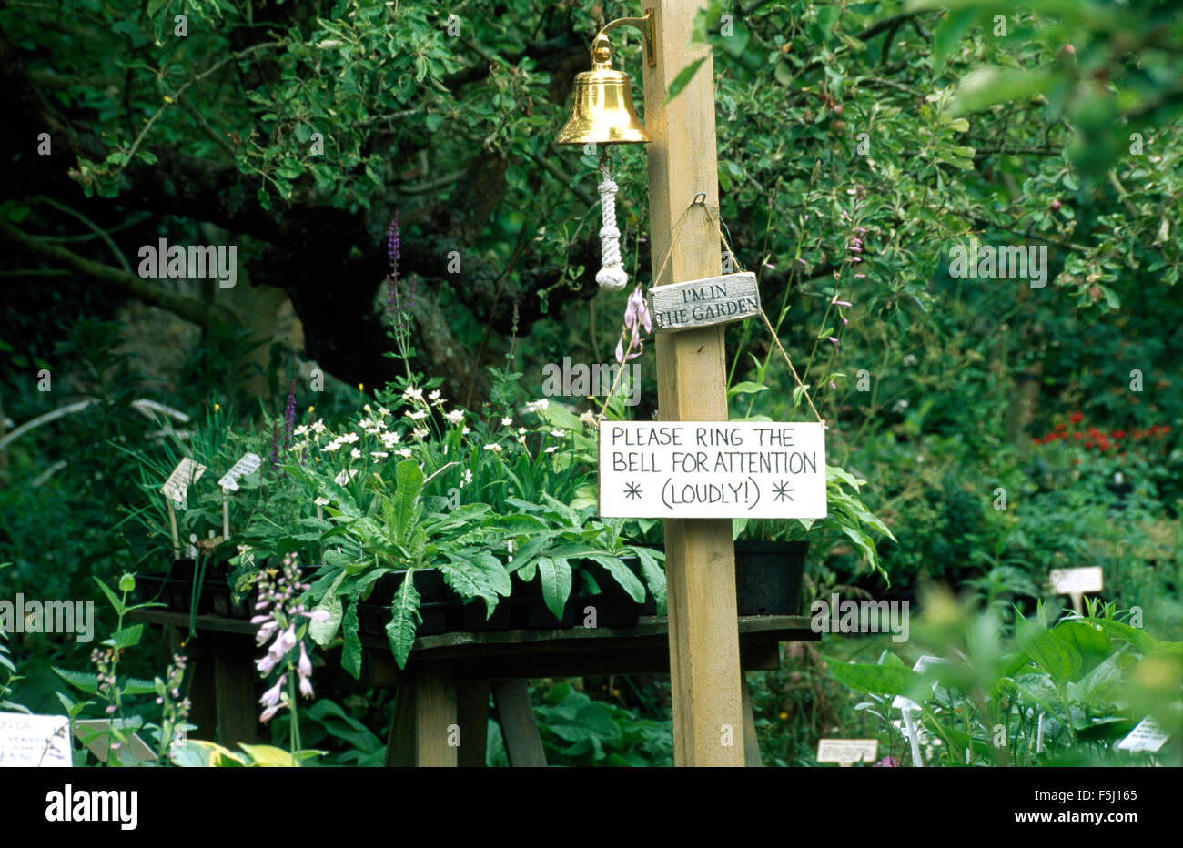 Brass bell on wooden post with signboards in front of a table with plants for sale Stock Photo