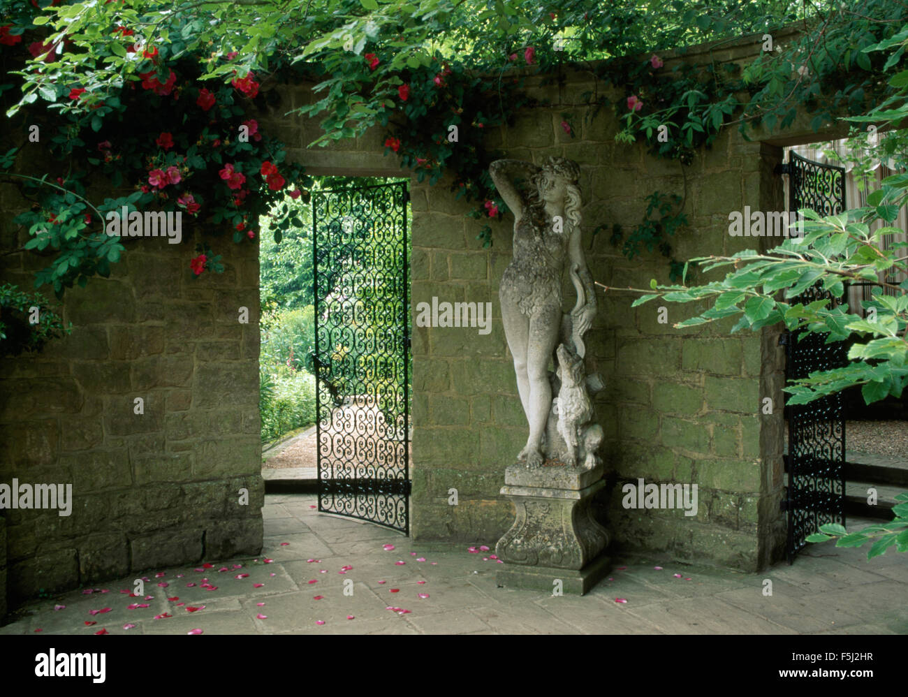 Classical stone statue between wrought iron gates in large walled