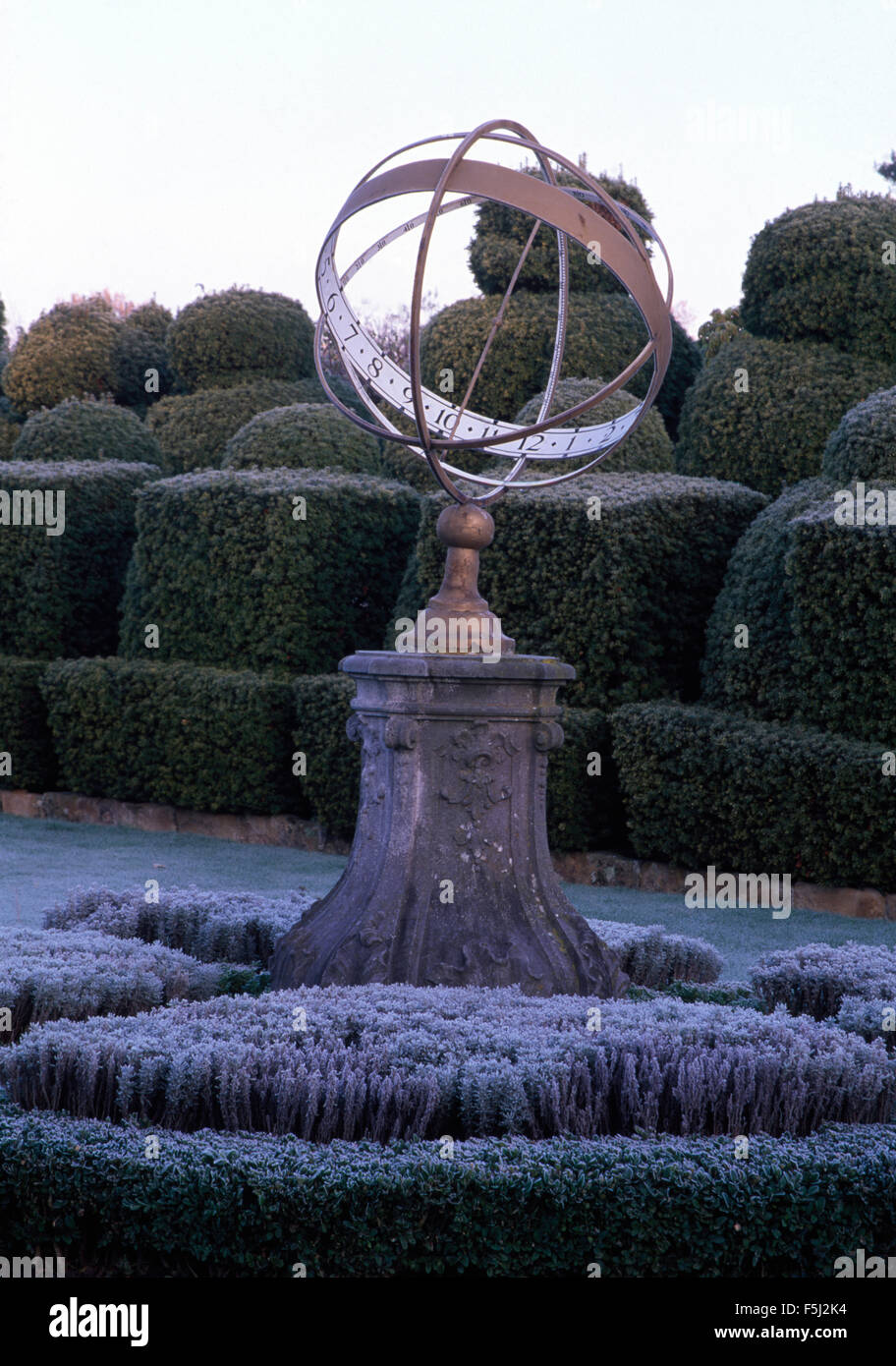 Armillary sphere on stone plinth in frosted knot garden with topiary Stock Photo