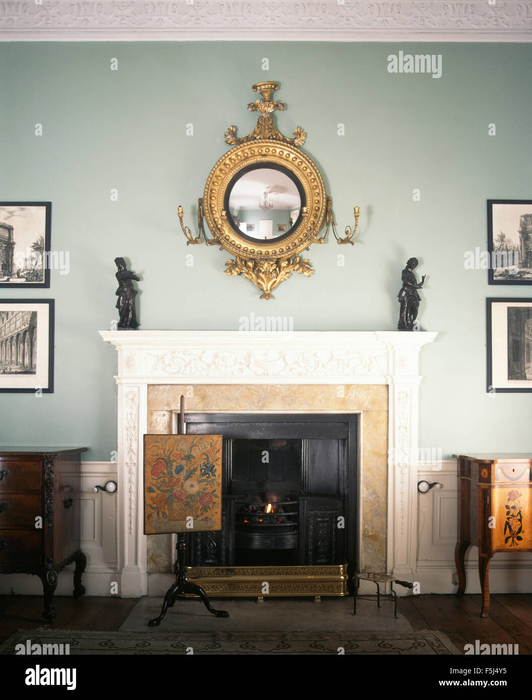 Antique Girandole mirror above fireplace with an antique fire-screen in pale blue Georgian dining room Stock Photo