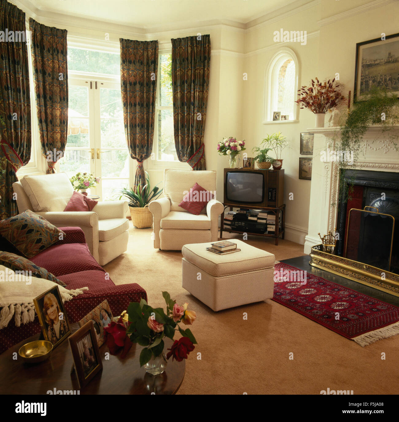 Cream armchairs and ottoman in an eighties townhouse sitting room with dark drapes on the French windows Stock Photo