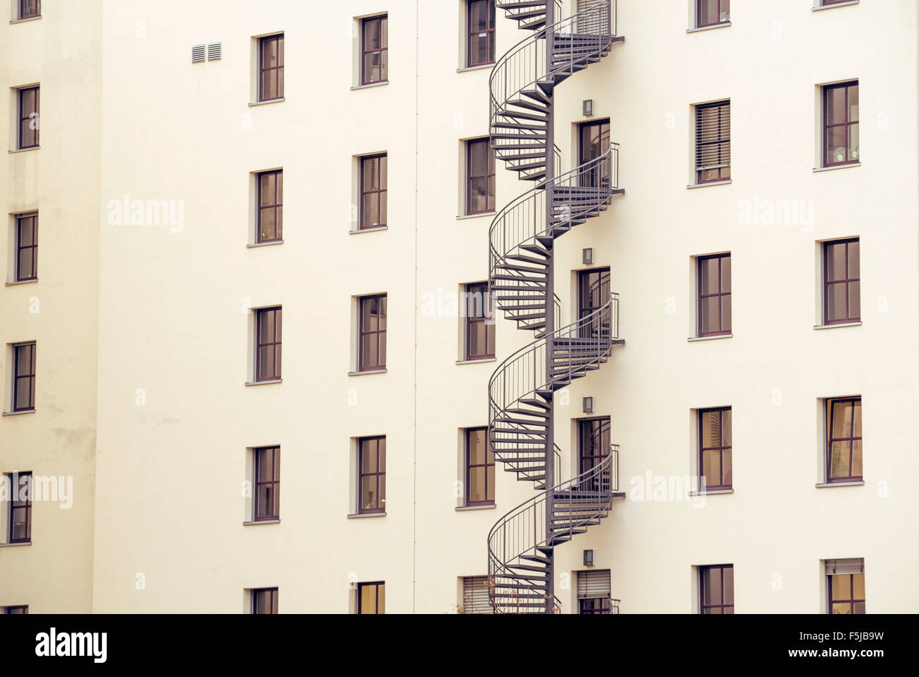 spiral metallic fire escape ladder at the backyard of modern building wall Stock Photo