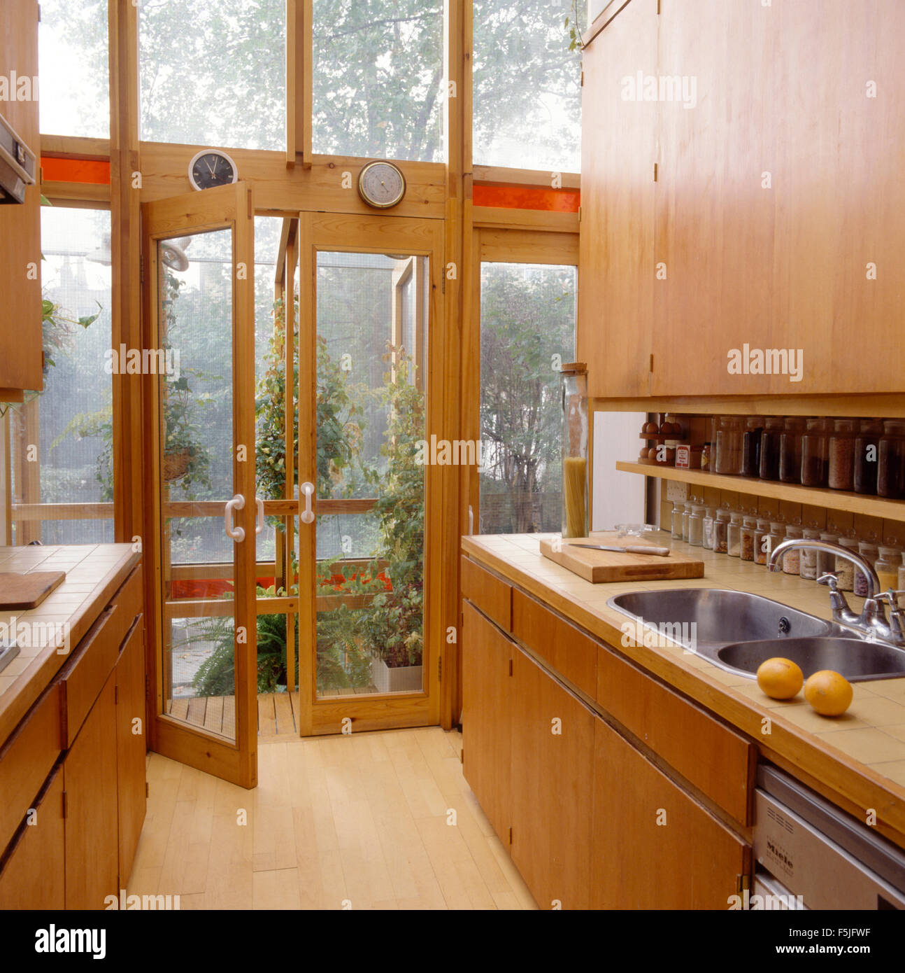 Wooden fitted units and glass doors in seventies kitchen extension Stock Photo