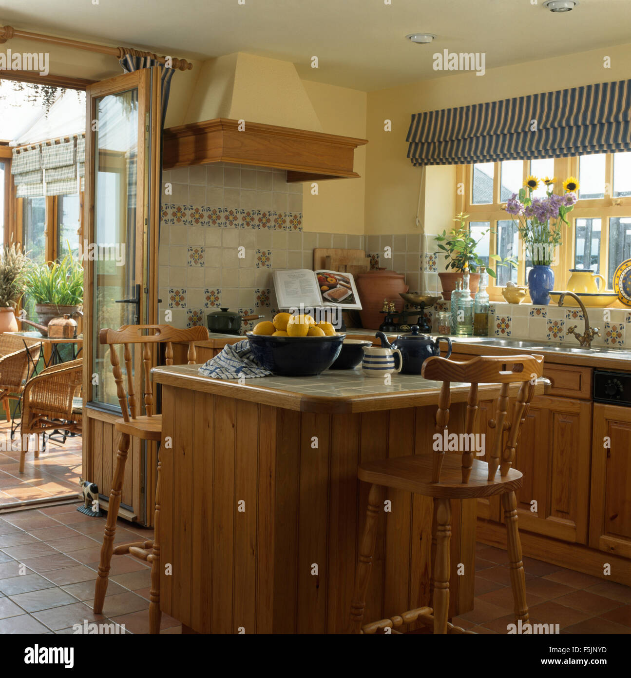 Pine stools at breakfast bar on island unit in a nineties kitchen with a striped blind on the window Stock Photo