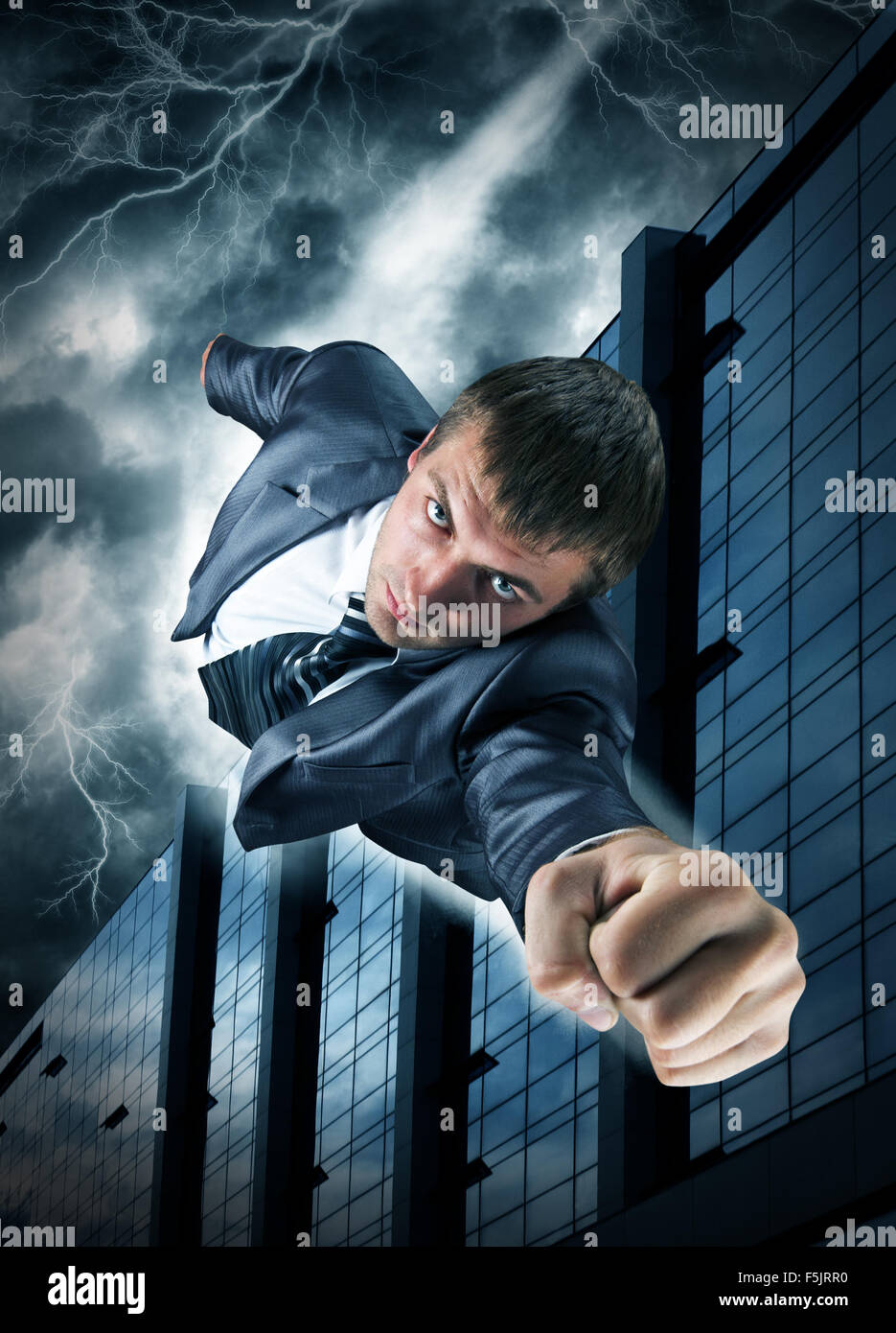 Superhero businessman flying over downtown in thunderstorm Stock Photo