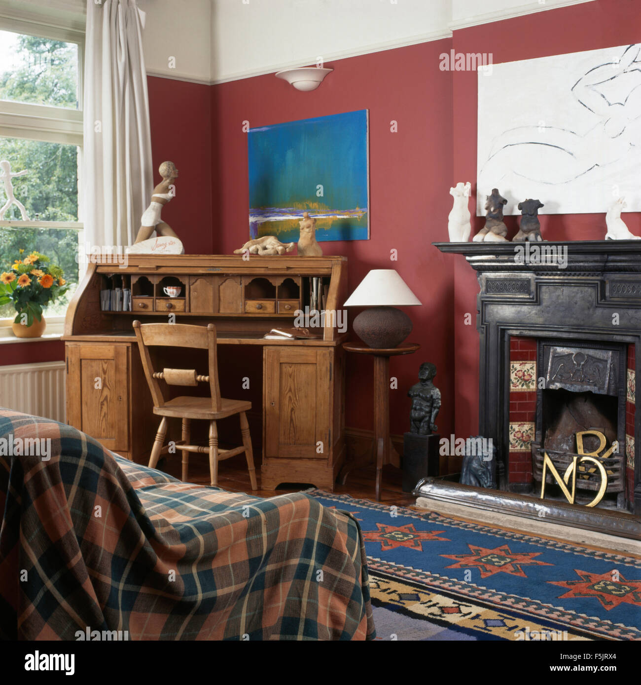 Plaid throw and old pine bureau in a red nineties living room with a black cast iron fireplace Stock Photo