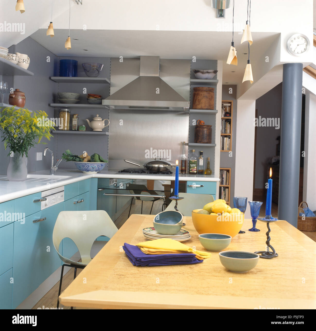 Lighted blue candles on pale wood table in gray kitchen extension with turquoise units and a stainless steel extractor Stock Photo