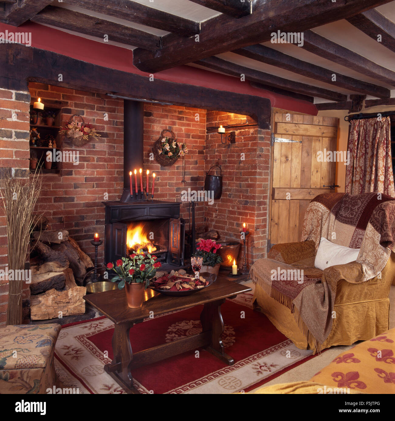 Cottage sitting room coffee table beside armchair in front of a wood burning stove in an exposed brick inglenook fireplace Stock Photo