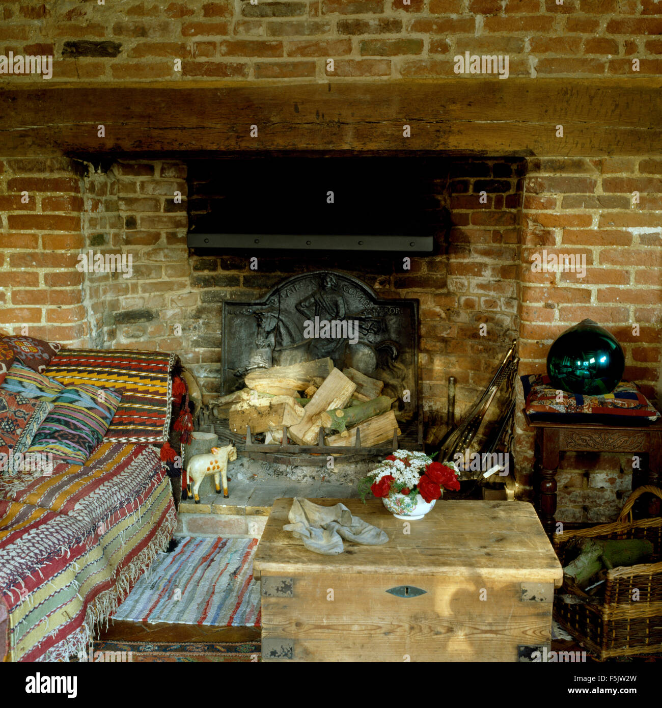 Old pine chest and sofa with patterned throws beside fireplace in dark old fashioned living room Stock Photo