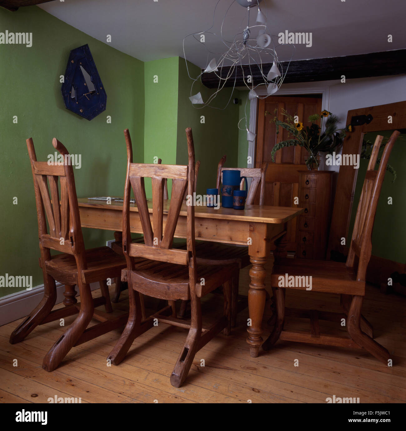 Carved rustic wooden chairs at a pine table in a nineties dining room with a twisted metal light fitting and wooden flooring Stock Photo