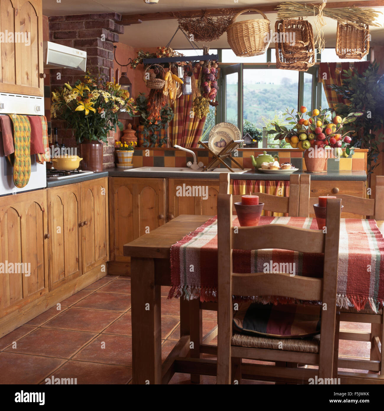 Rustic wooden chairs at table with checked cloth in a country kitchen with pine doors on fitted