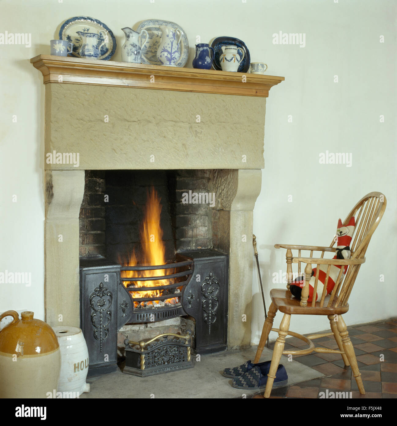 Windsor chair beside a stone fireplace with a lighted fire in a country dining room Stock Photo