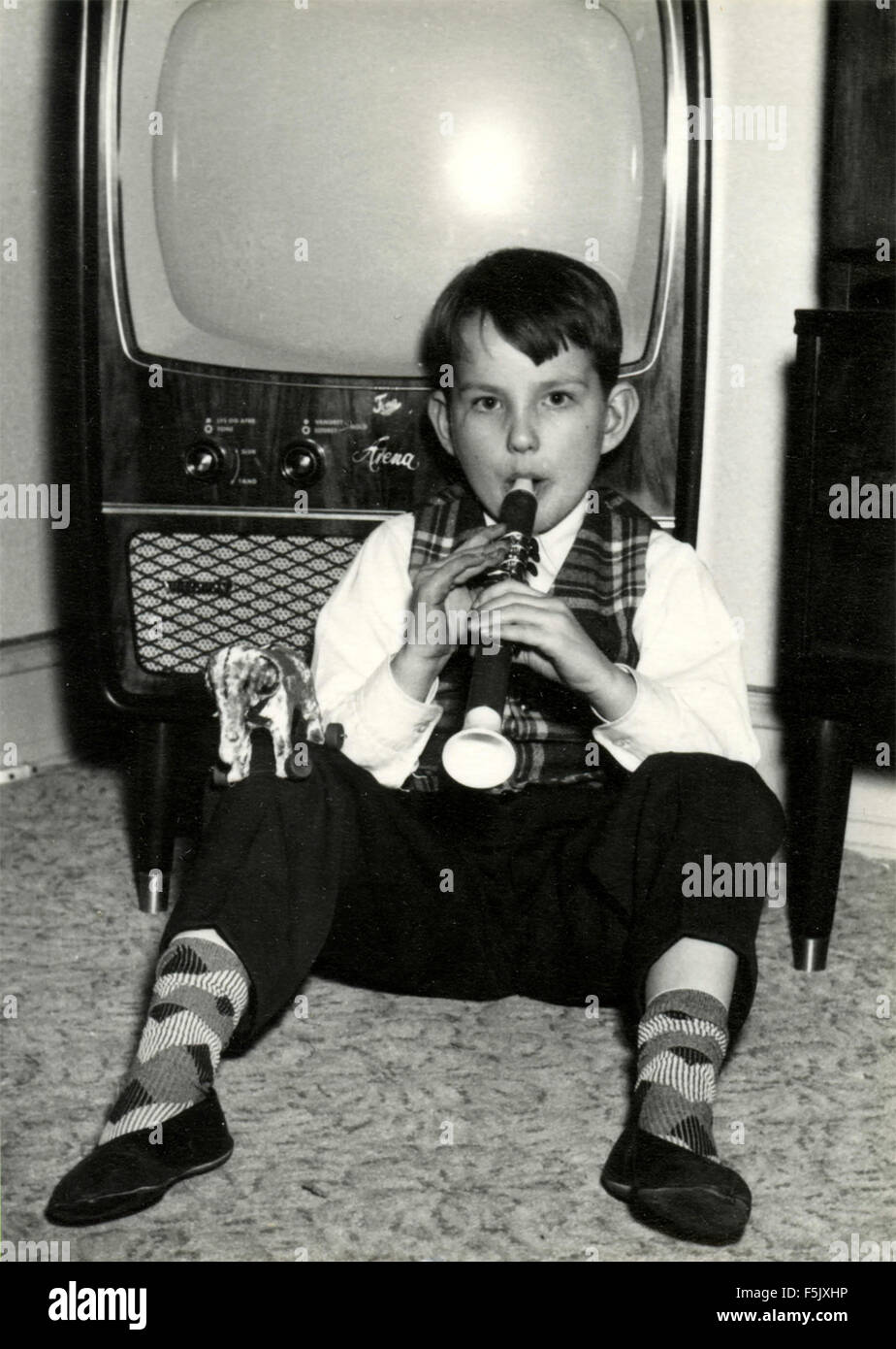A child plays the flute next to the TV Stock Photo
