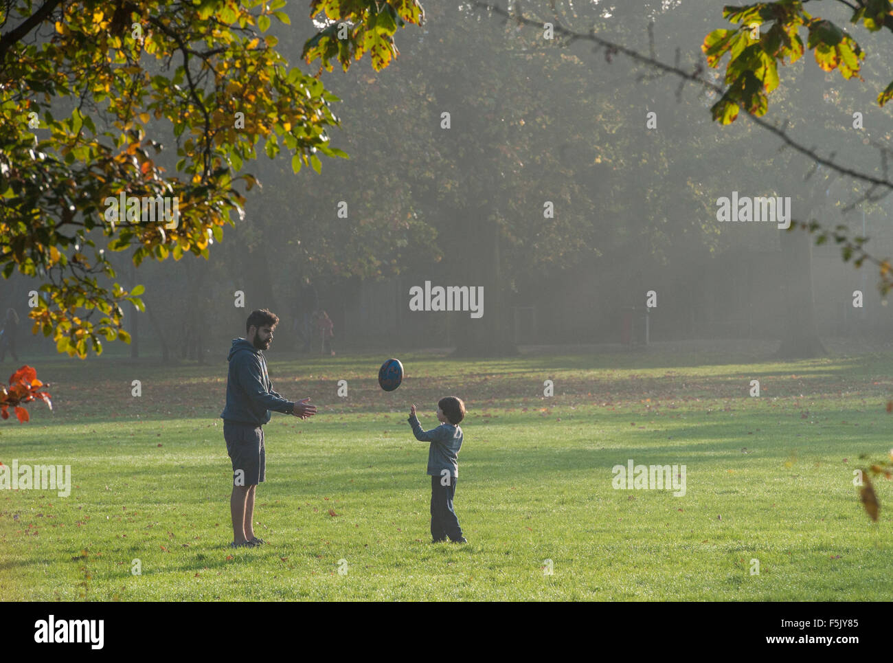 A father and son play rugby together in a park Stock Photo