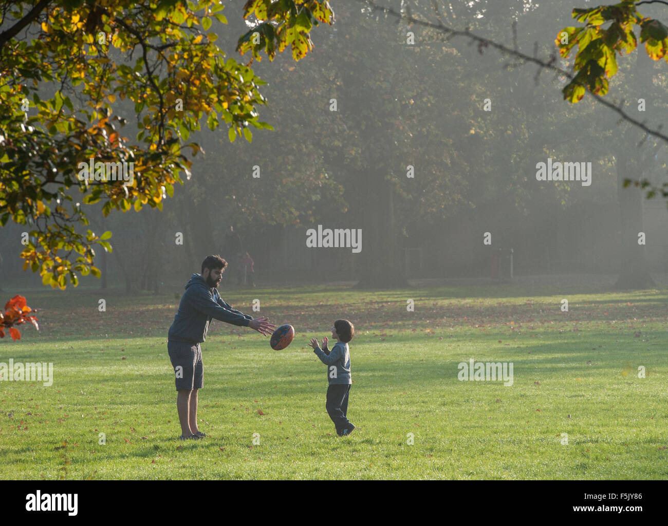 A father and son play rugby together in a park Stock Photo
