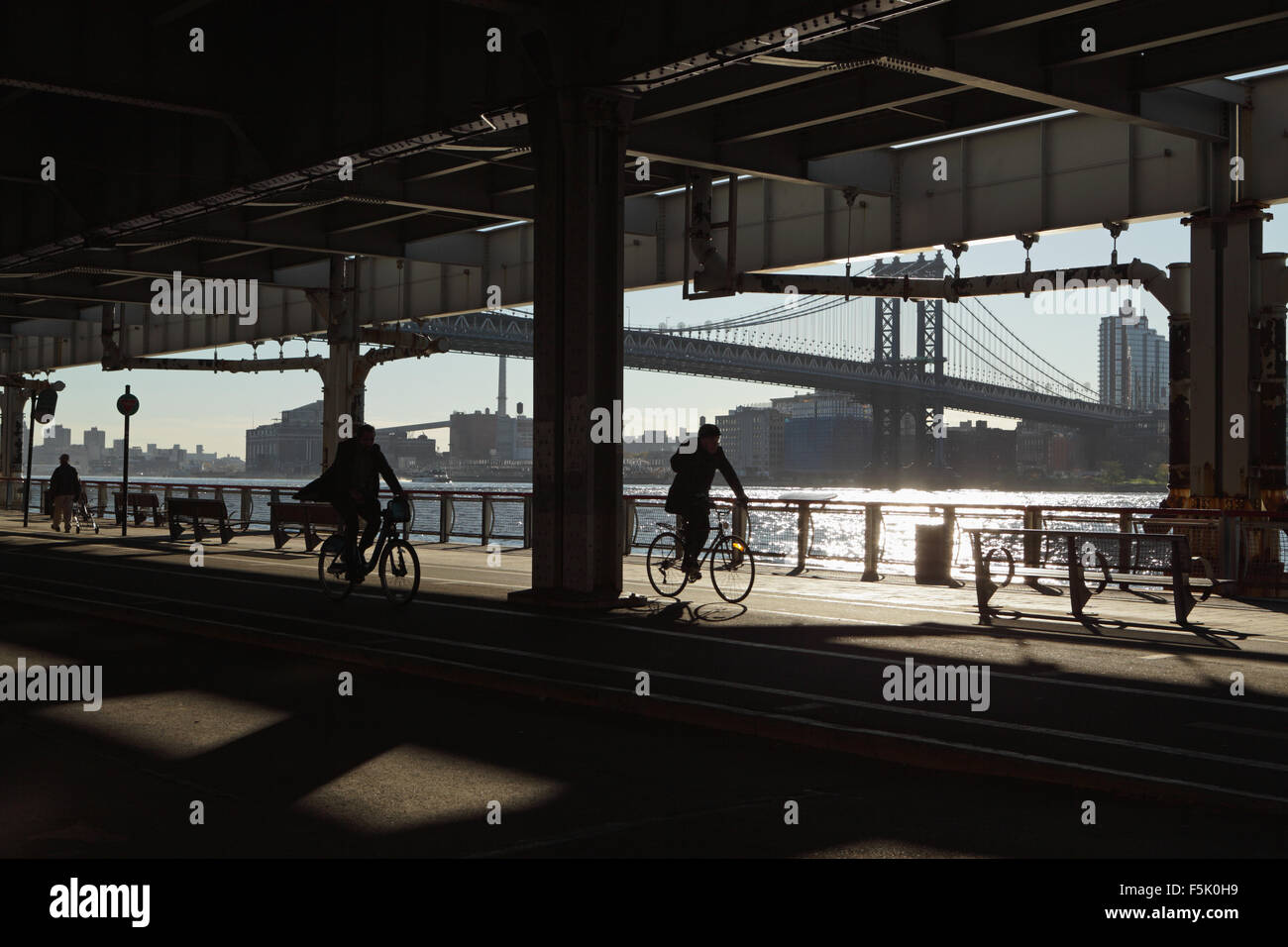 Two men cycle and another walks along the East River Esplanade, New York, under the Roosevelt East River Drive overpass Stock Photo