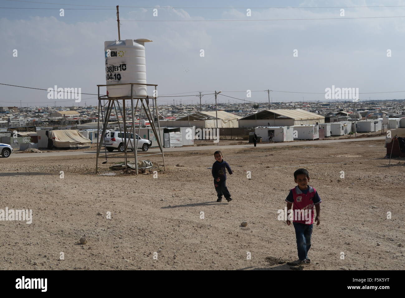 Two refugee boys play in the dust near a water tower at the highest point at Zaatari refugee camp in Jordan Stock Photo