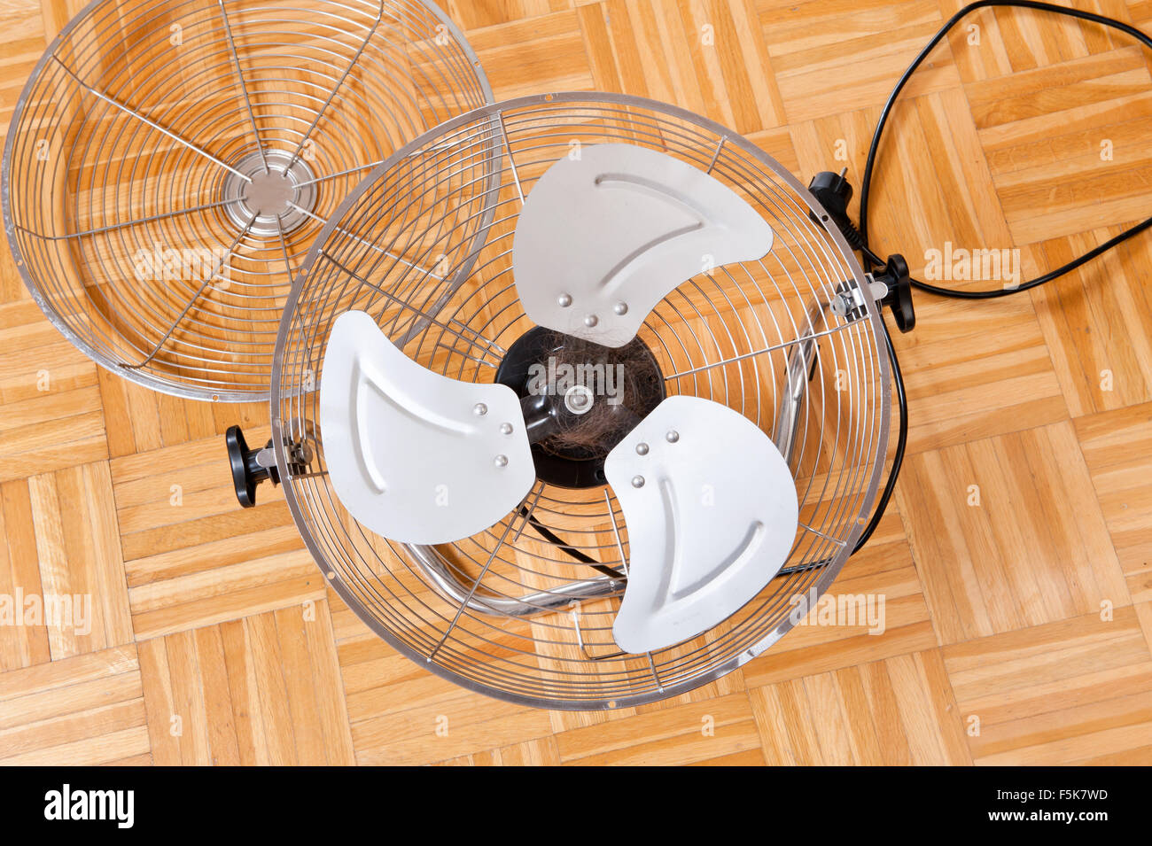 Tangled human hair in a fan, household electric floor chrome fan machine with turning vanes making comfortable airflow, cleaning Stock Photo