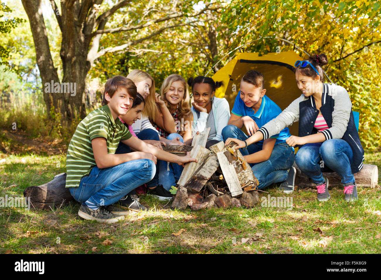 Happy teens sett up bonfire together on campsite Stock Photo