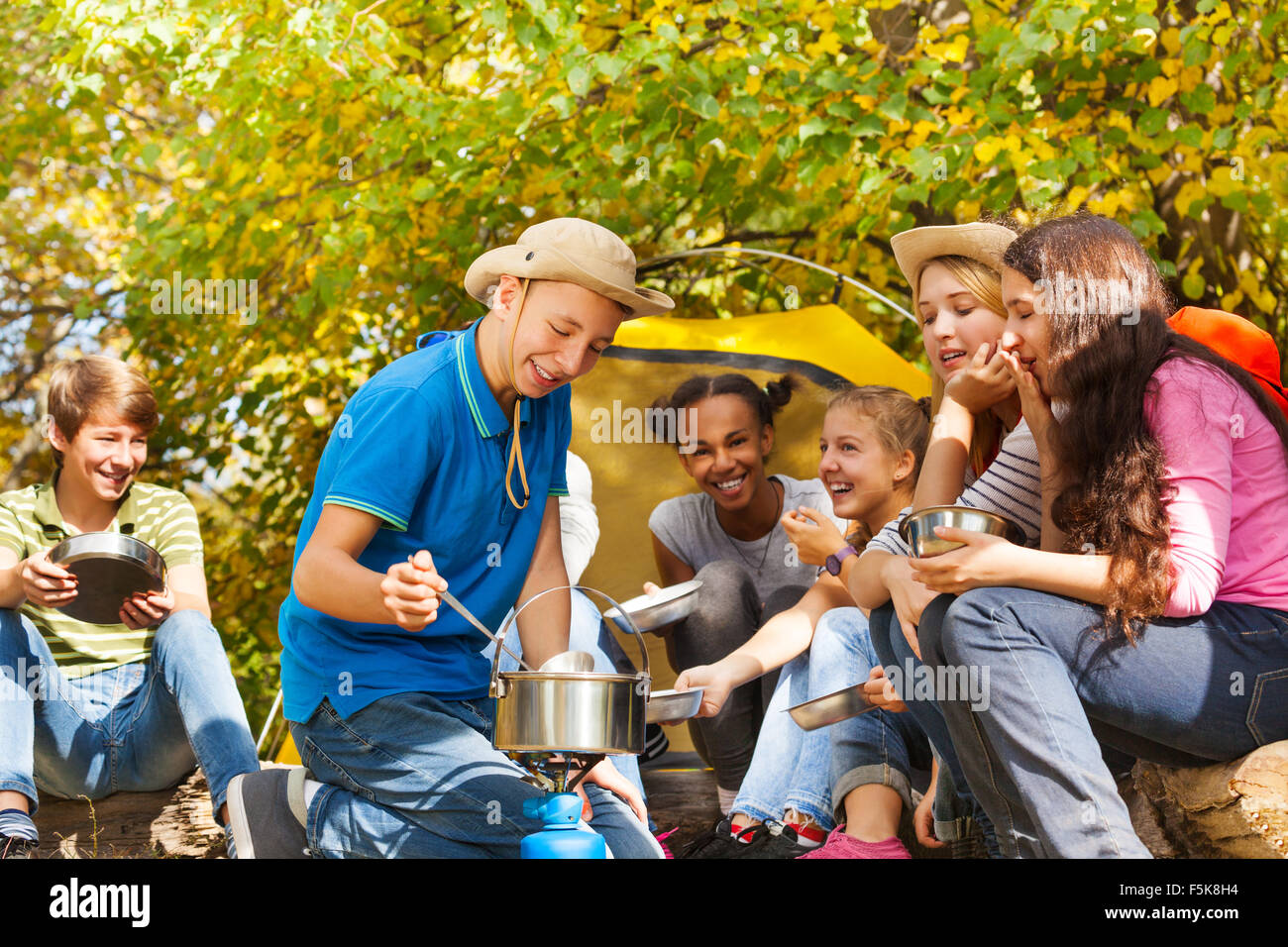 Boy cooks soup in pot for friends at campsite Stock Photo