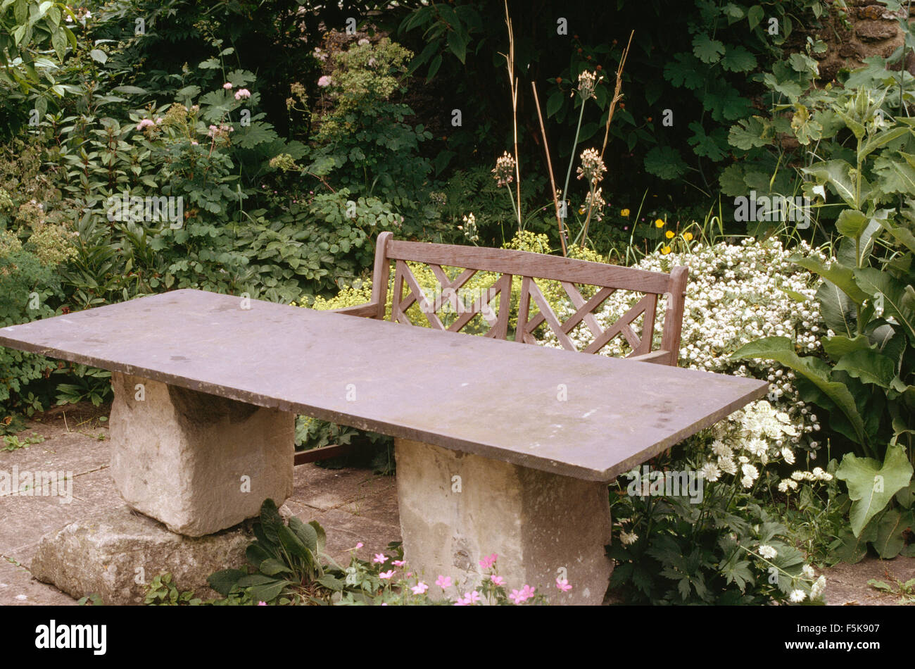 Garden table made from slate top on rough stone plinths on a patio edged with white perennials and alchemilla mollis Stock Photo