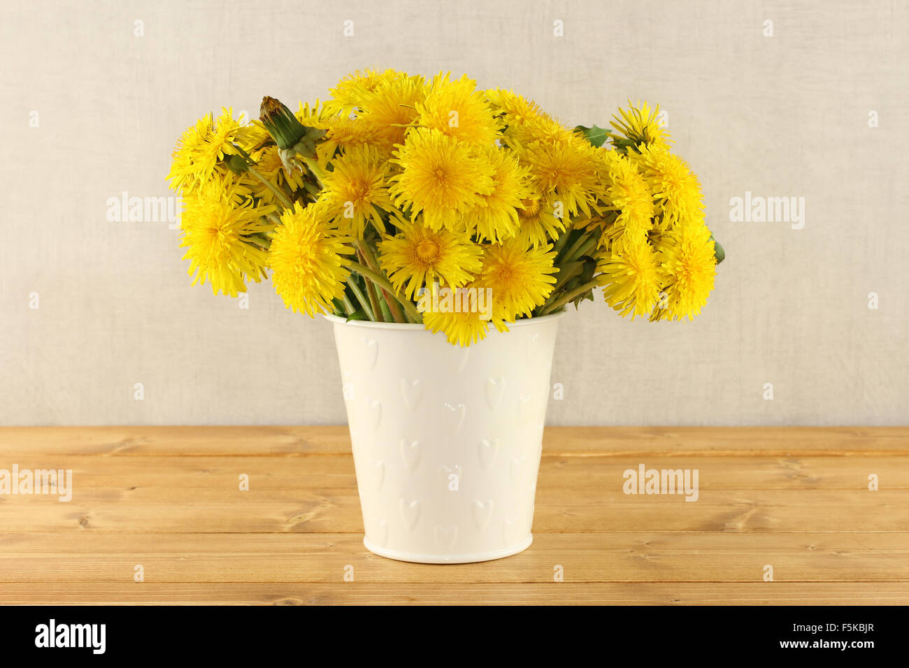 Bouquet of dandelions in small white bucket on light brown wooden table ...