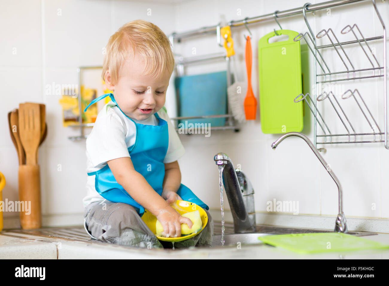 Cute child boy 2 years old washing up in kitchen Stock Photo