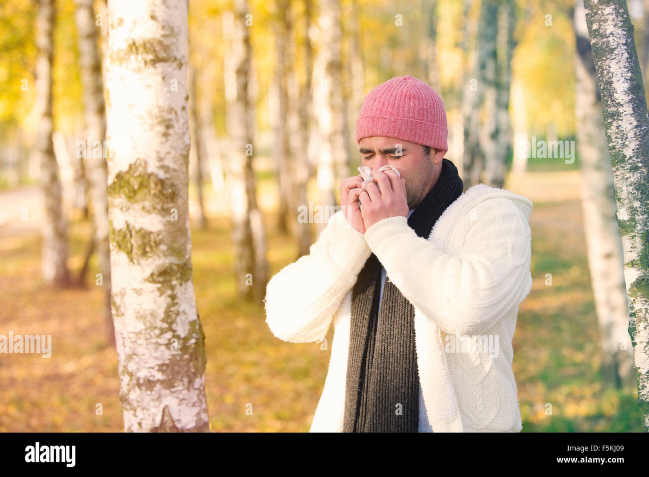 man standing by trees in fall and blowing his nose Stock Photo