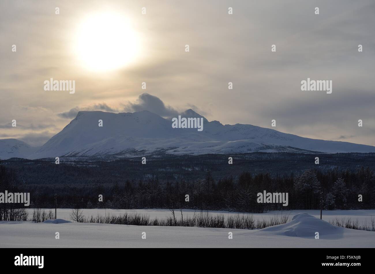strong sunshine over snowy mountain peak as strong wind blows the snow ...