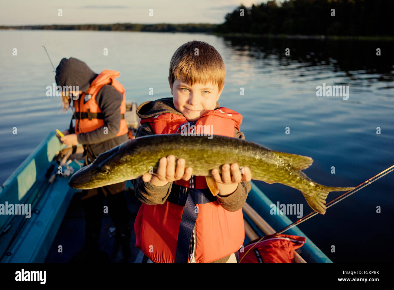 Sweden, Smaland, Tjust archipelago, Vastervik, Hasselo, Boy (10-11) on boat showing caught fish with girl in background (8-9) Stock Photo