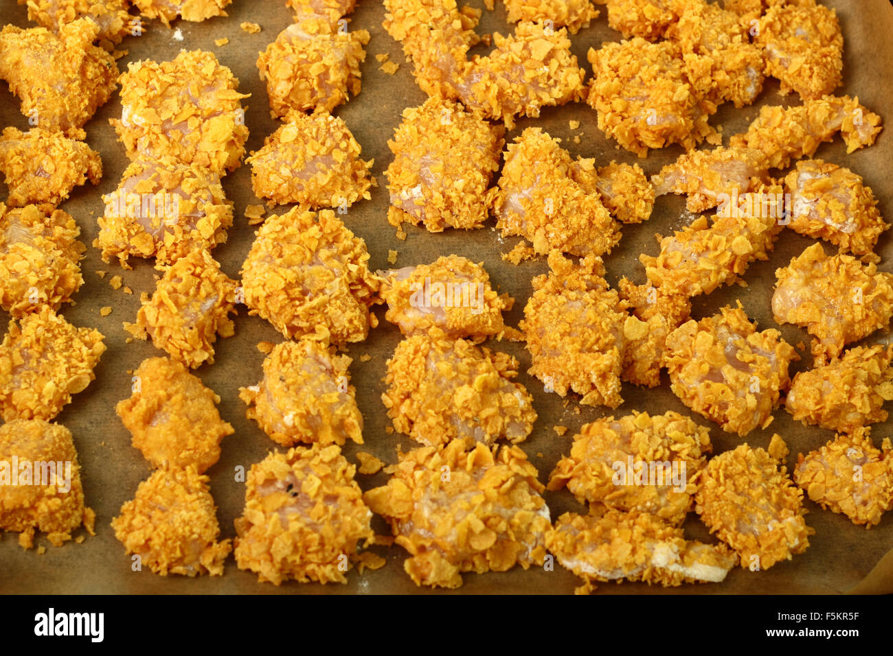 Raw breaded in corn flakes chicken fillet on baking sheet. Making oven
