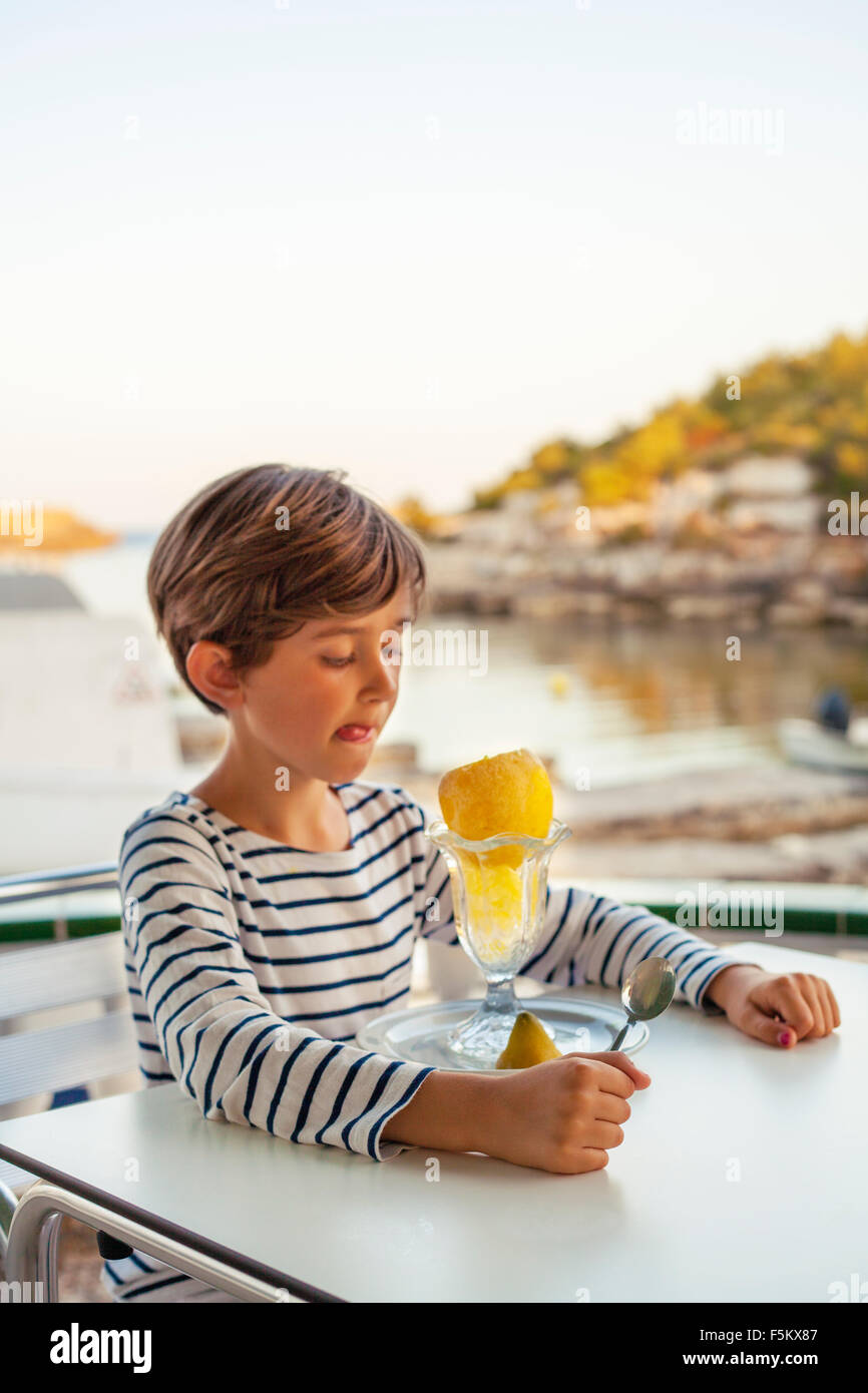 Spain, Menorca, Boy (6-7) licking lips while looking at orange Stock Photo
