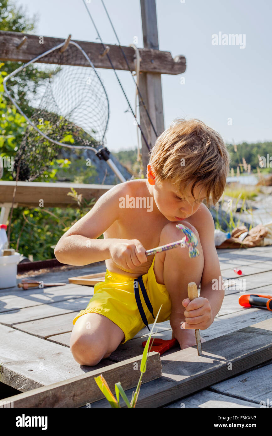 Sweden, Uppland, Runmaro, Barrskar, Boy (4-5) repairing wooden deck Stock Photo