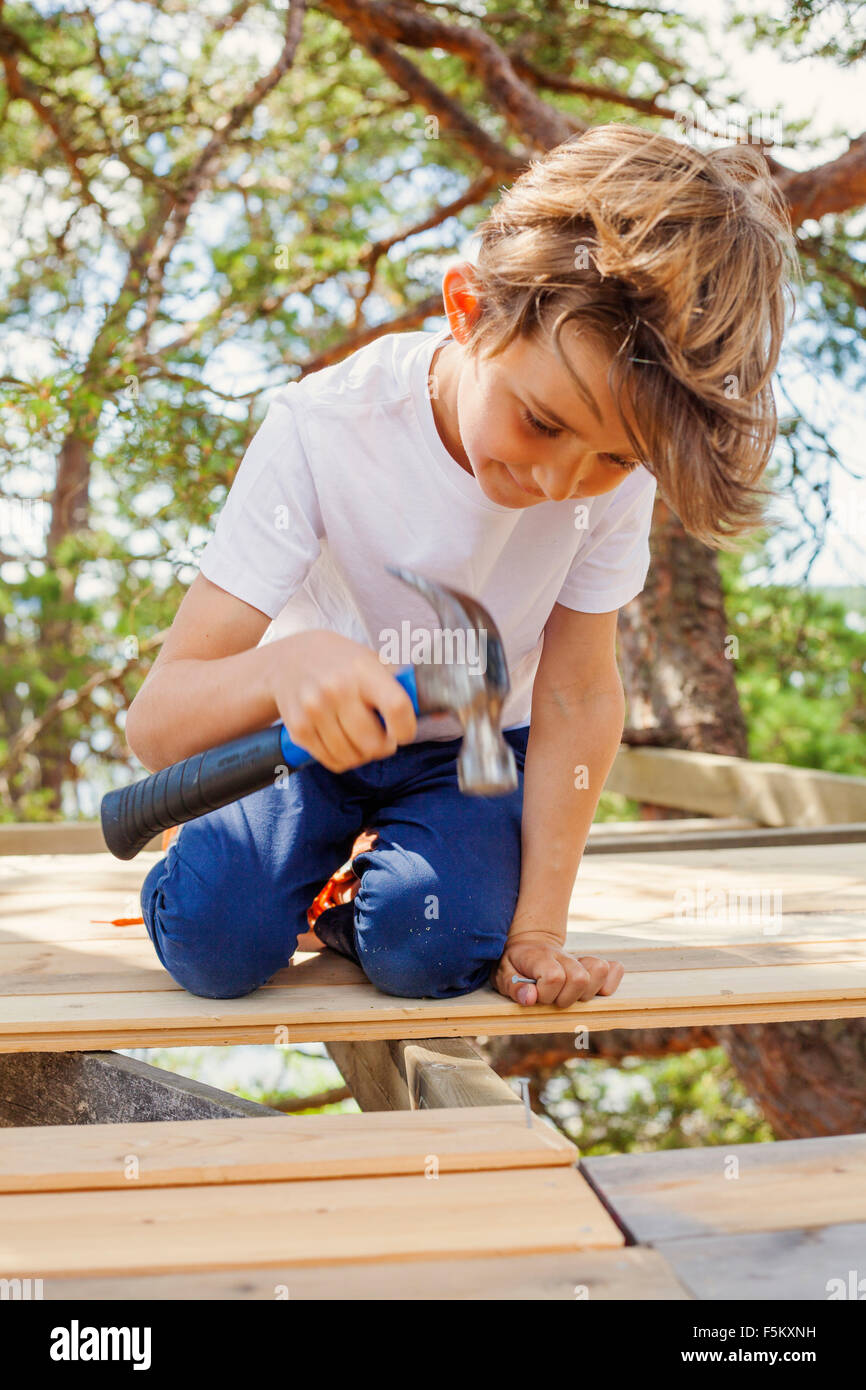 Sweden, Uppland, Runmaro, Barrskar, Portrait of boy (6-7) pounding hammer Stock Photo