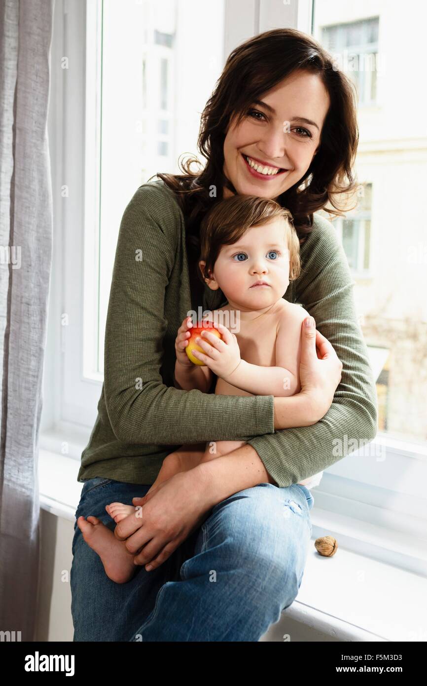 Mother holding baby boy, sitting in window Stock Photo